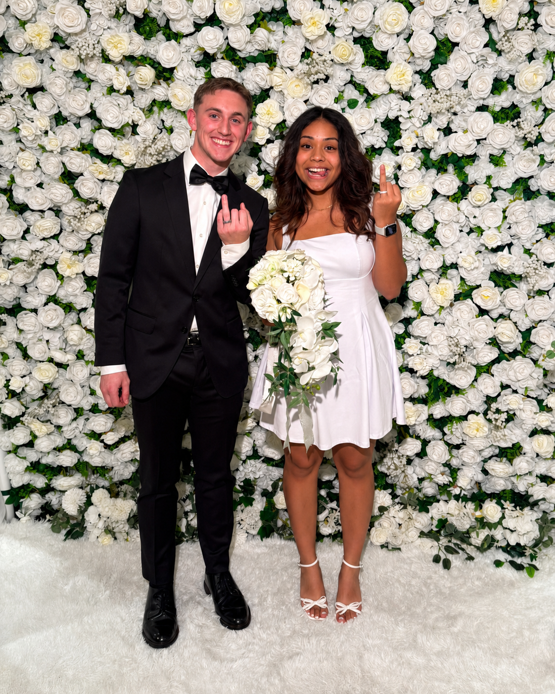Newly married couple displaying their wedding rings in front of the white floral wall at Dallas Wedding Officiants