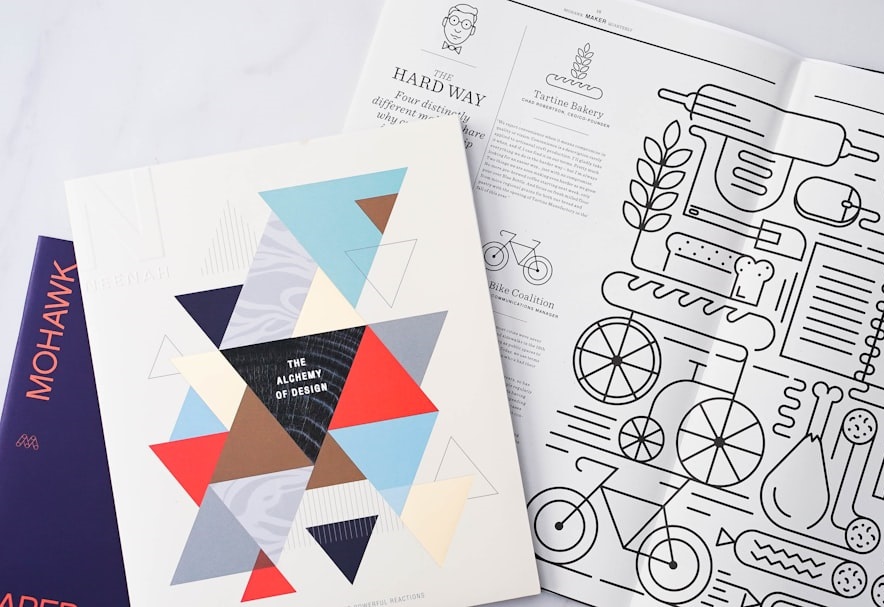 A collection of design magazines and brochures displayed on a flat surface. The cover features geometric patterns and bold typography, alongside an illustrated layout related to baking and cycling. Bath Digital Marketing Agency