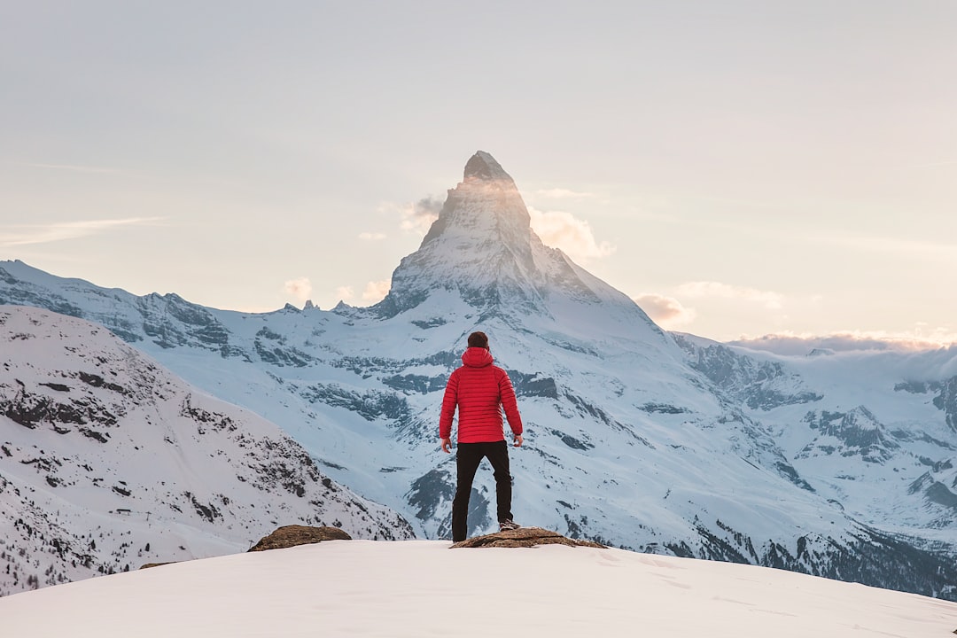 Person in a red jacket standing on a snowy peak, gazing at the Matterhorn mountain in the distance Bath Digital Marketing Agency