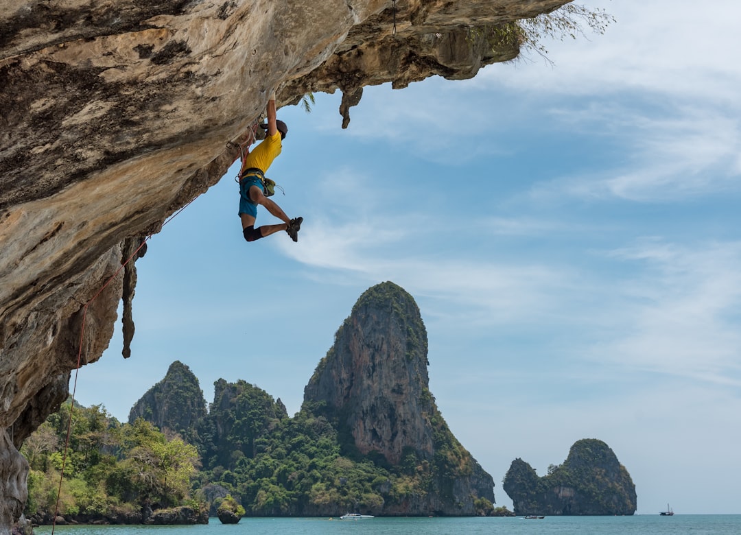 A climber hanging from a rocky overhang against a backdrop of cliffs and islands under a blue sky. Bath Digital Marketing Agency