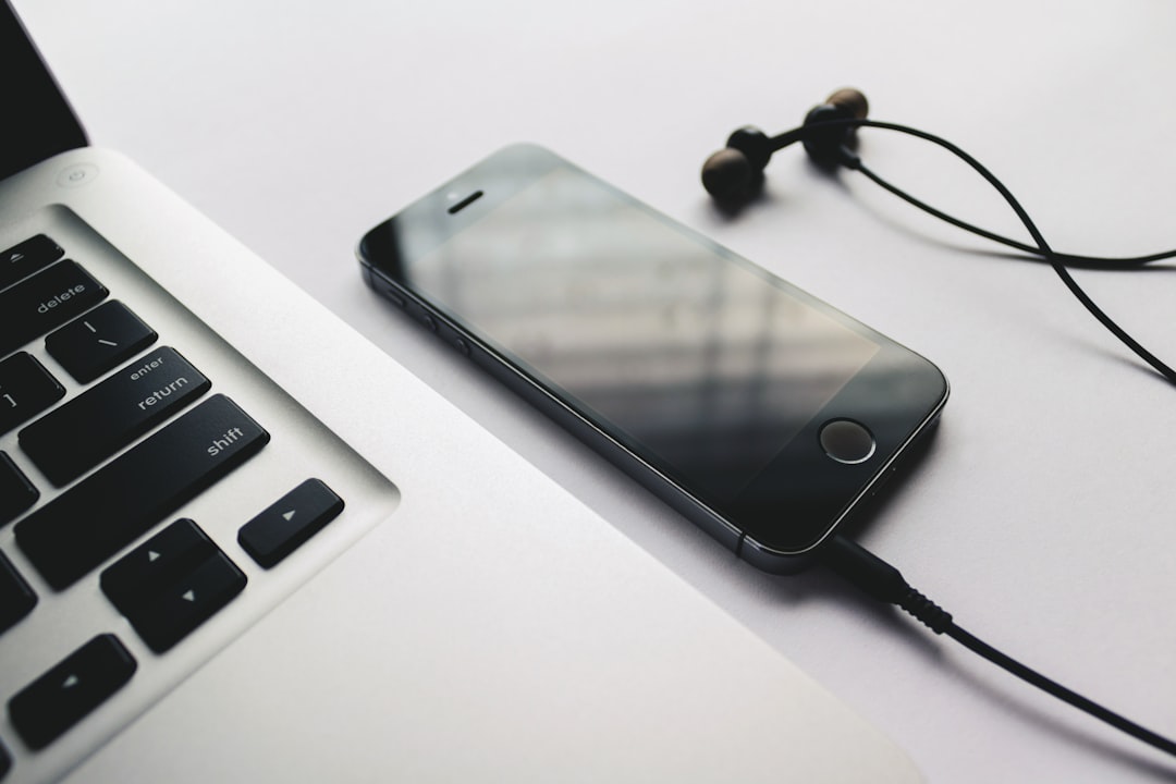 A smartphone connected to headphones resting on a desk beside a laptop keyboard, highlighting a casual workspace setup. Bath Digital Marketing Agency