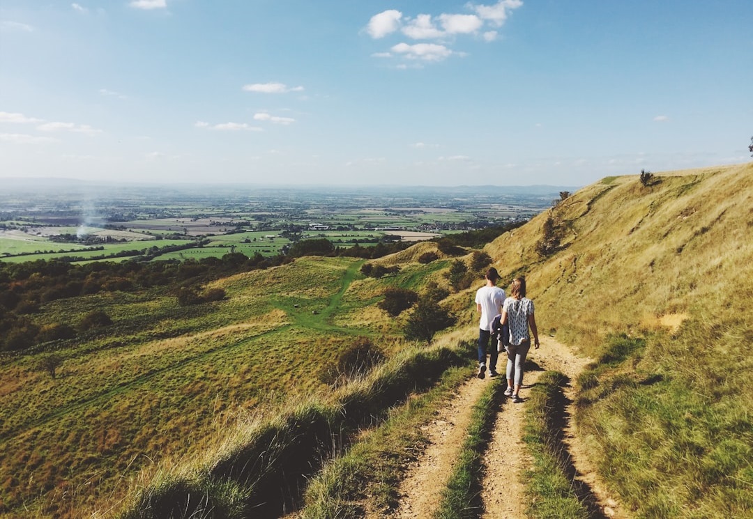 Two people walking along a grassy path on a hillside, overlooking a scenic landscape with fields and distant hills under a blue sky. Bath Digital Marketing Agency