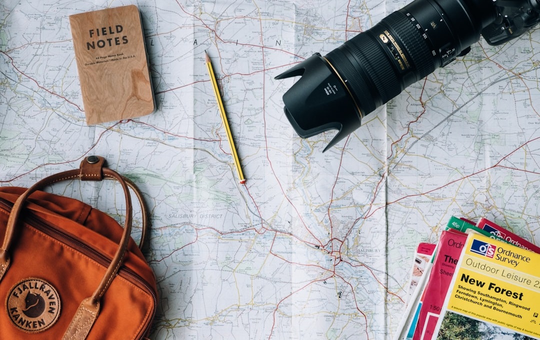 A flat lay of a travel setup featuring a detailed map, a pencil, a camera lens, a notebook, and various guidebooks, arranged on a rustic surface. Bath Digital Marketing Agency