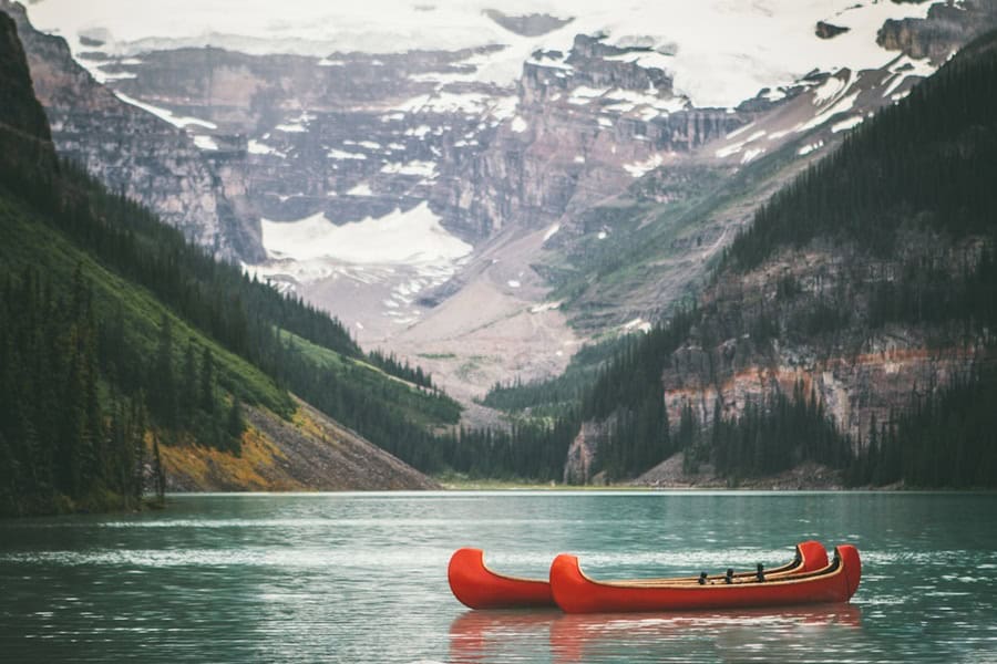 Two red canoes floating on a serene lake, surrounded by lush greenery and towering mountains. Snow-capped peaks are visible in the background, creating a picturesque landscape. Bath Digital Marketing Agency