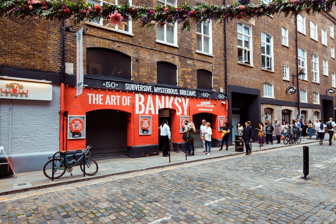 Street scene showcasing the entrance to "The Art of Banksy" exhibition, with visitors and bicycles nearby. Bath Digital Marketing Agency