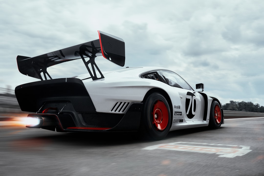 A high-performance racing car with a large rear wing speeding down a track, emitting exhaust flames under a cloudy sky. Bath Digital Marketing Agency