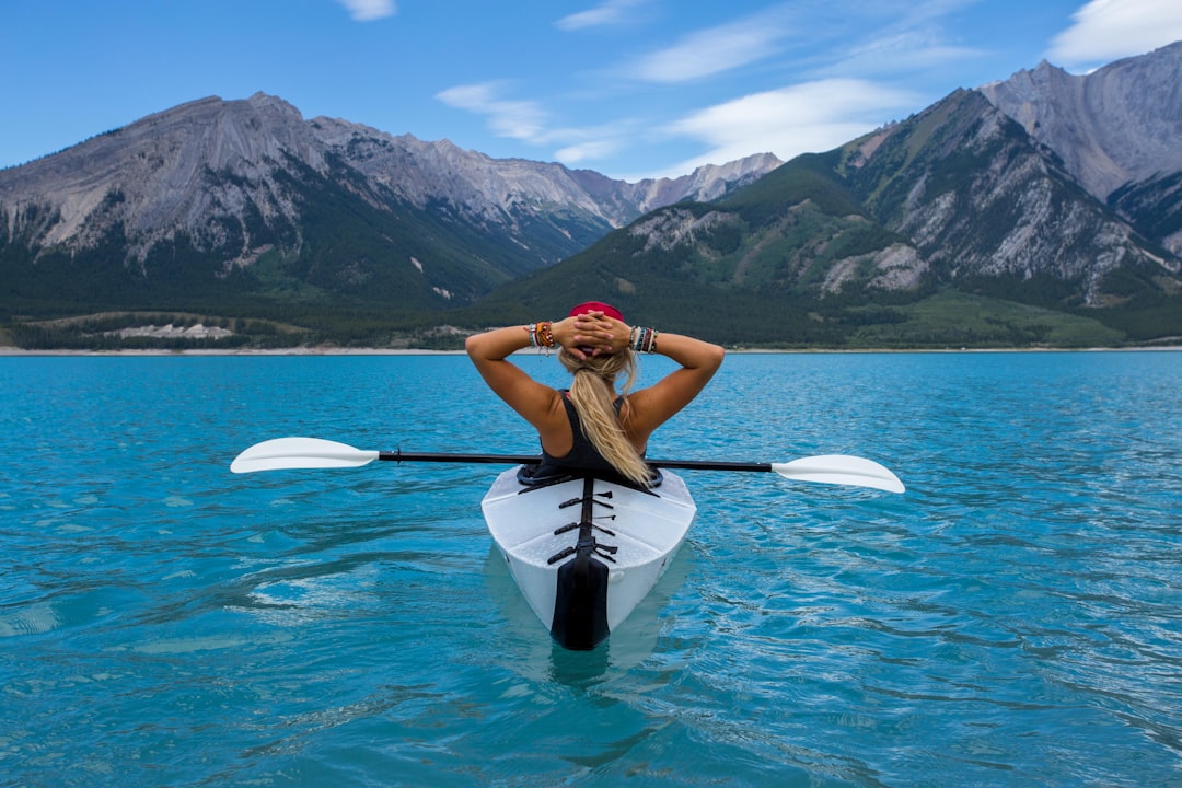 A person in a kayak on a turquoise lake, facing mountains under a blue sky. Bath Digital Marketing Agency