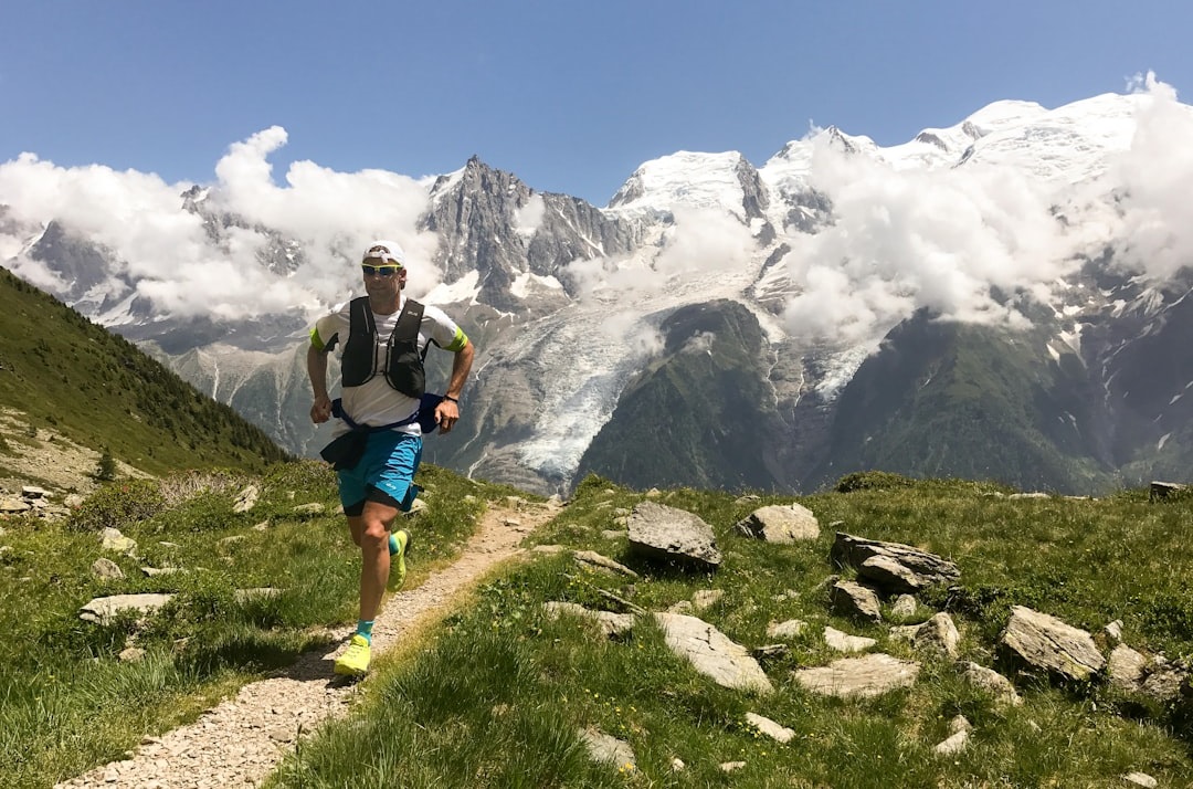 A runner in athletic gear navigating a rocky trail through a lush landscape, with snow-capped mountains and clouds in the background. Bath Digital Marketing Agency