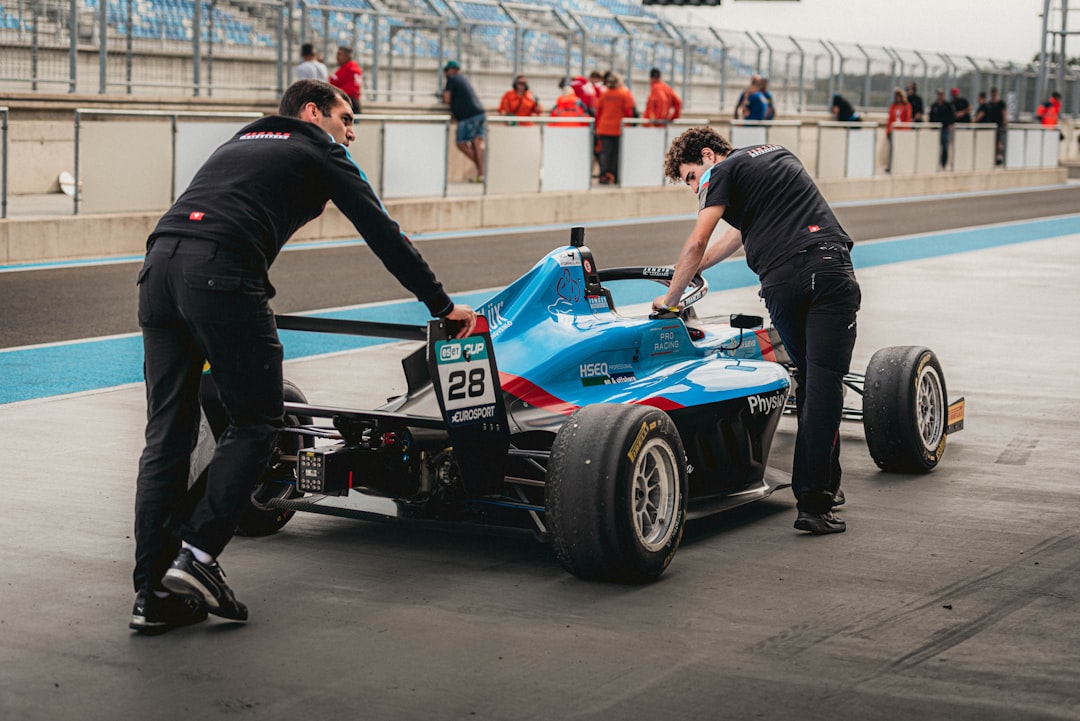 Two mechanics pushing a blue racing car in a pit area, preparing for a race, with team members in the background. Bath Digital Marketing Agency