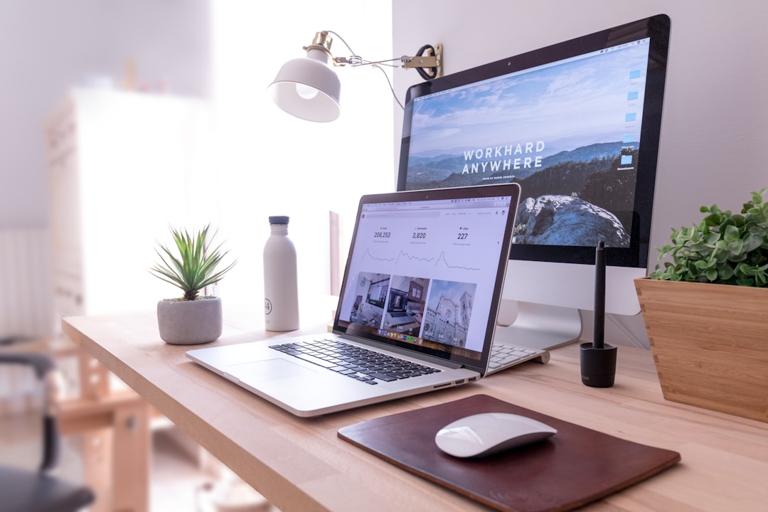A modern workspace featuring a laptop and a desktop computer with a motivational wallpaper, accompanied by a plant, a water bottle, and a mouse on a wooden desk Bath Digital Marketing Agency.
