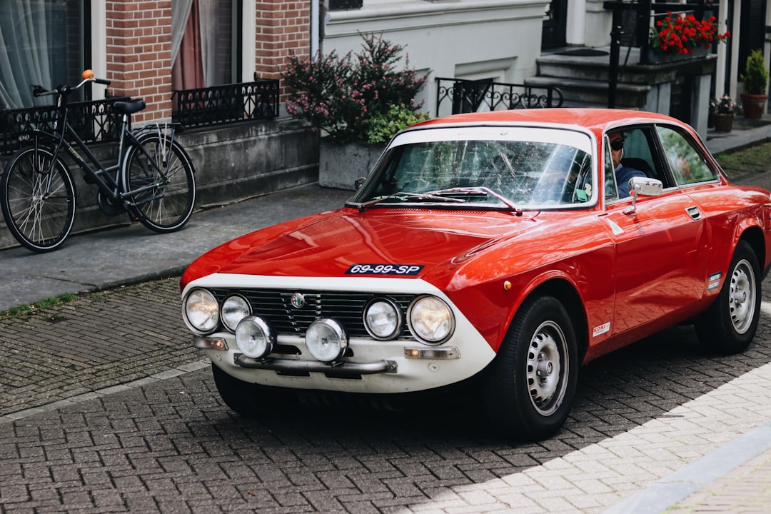 A vintage red sports car parked on a cobblestone street, featuring distinctive front headlights. In the background, a bicycle and potted plants add to the charming urban scene. Bath Digital Marketing Agency
