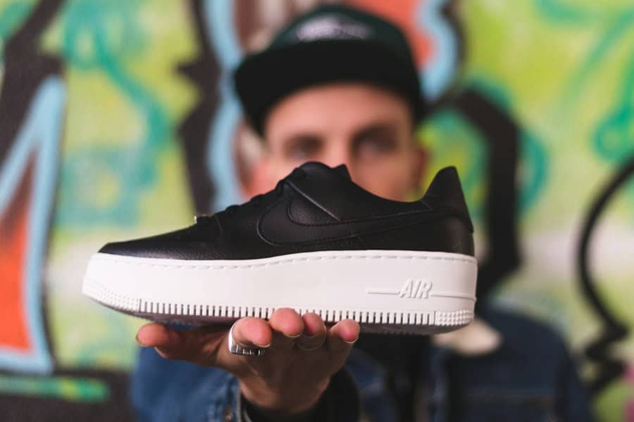 A person holding a black Nike sneaker with a white sole in front of a vibrant graffiti background, showcasing the shoe's design and style. Bath Digital Marketing Agency