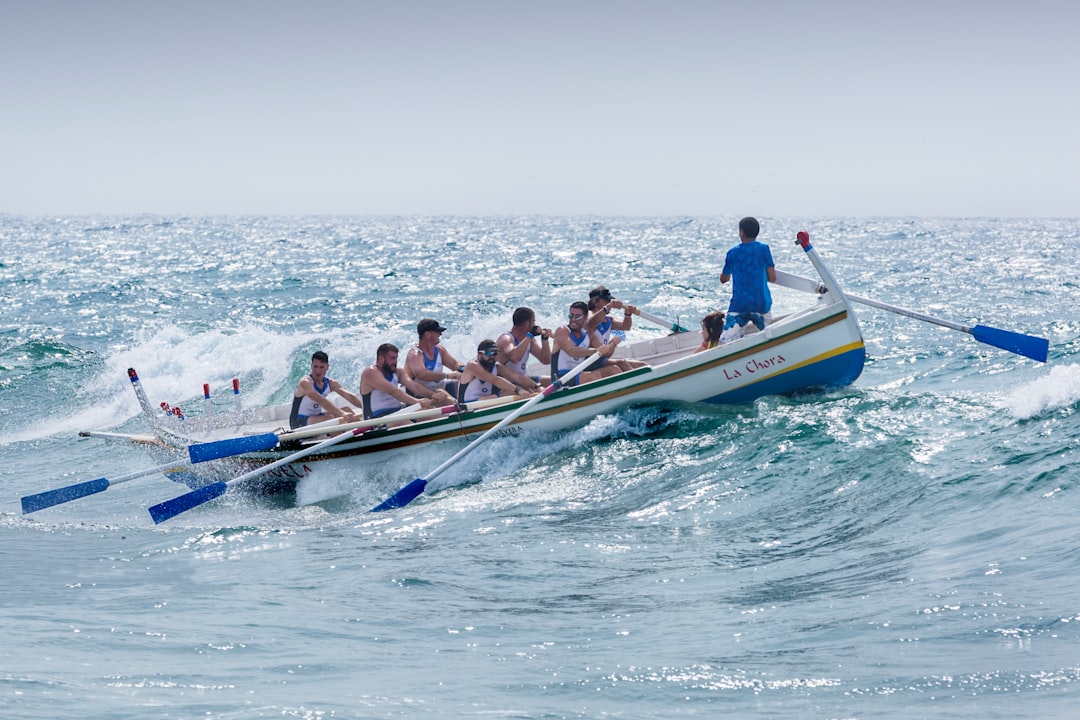 A crew of rowers in a boat, energetically paddling through choppy waters, with a coach steering at the back. Bath Digital Marketing Agency