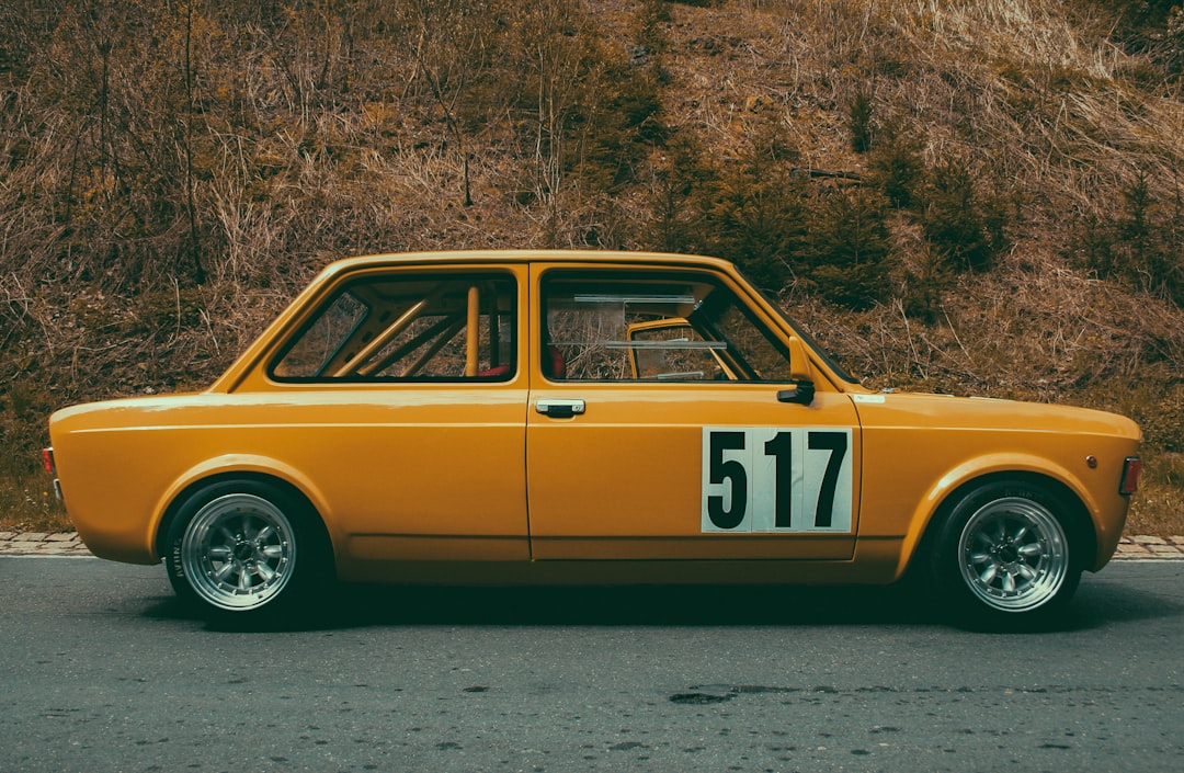 A vintage yellow car with racing number 517, featuring distinctive wheels, parked on a road with a backdrop of trees and dry grass.  Bath Digital Marketing Agency