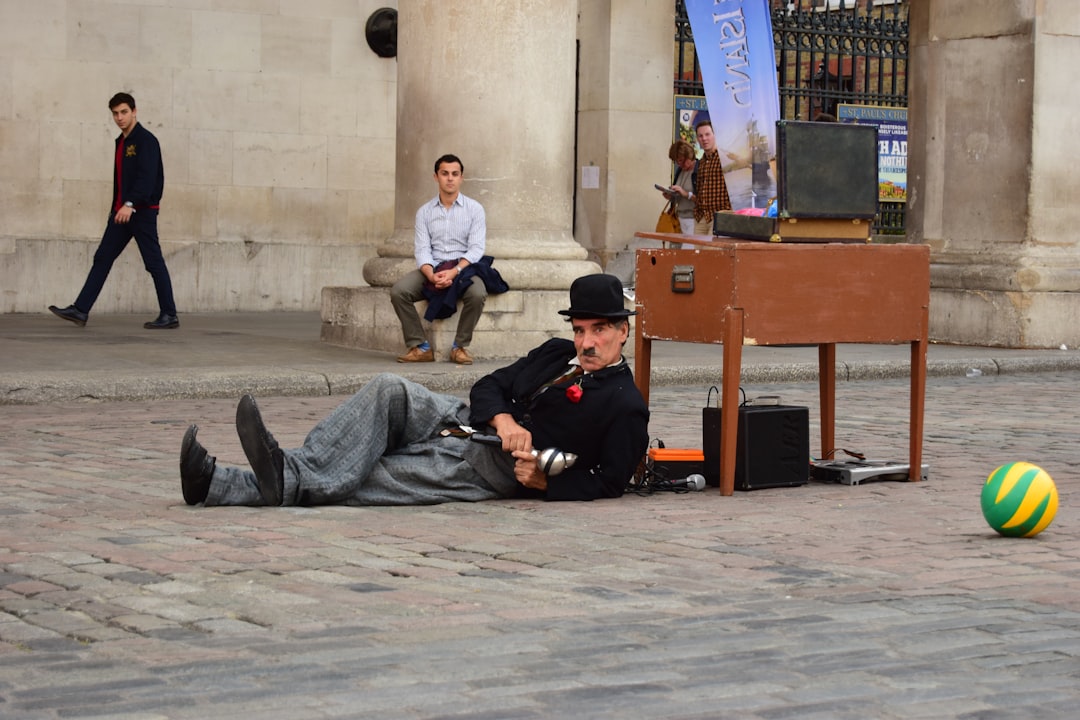 A street performer in a bowler hat lying on the ground, playing a musical instrument beside an old-fashioned music box, with passers by in the background. Bath Digital Marketing Agency