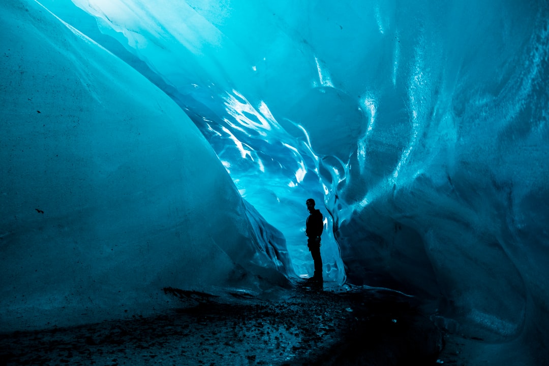A person stands inside a stunning ice cave, illuminated by blue light reflecting off the walls. The smooth ice formations create a dramatic and enchanting atmosphere. Bath Digital Marketing Agency