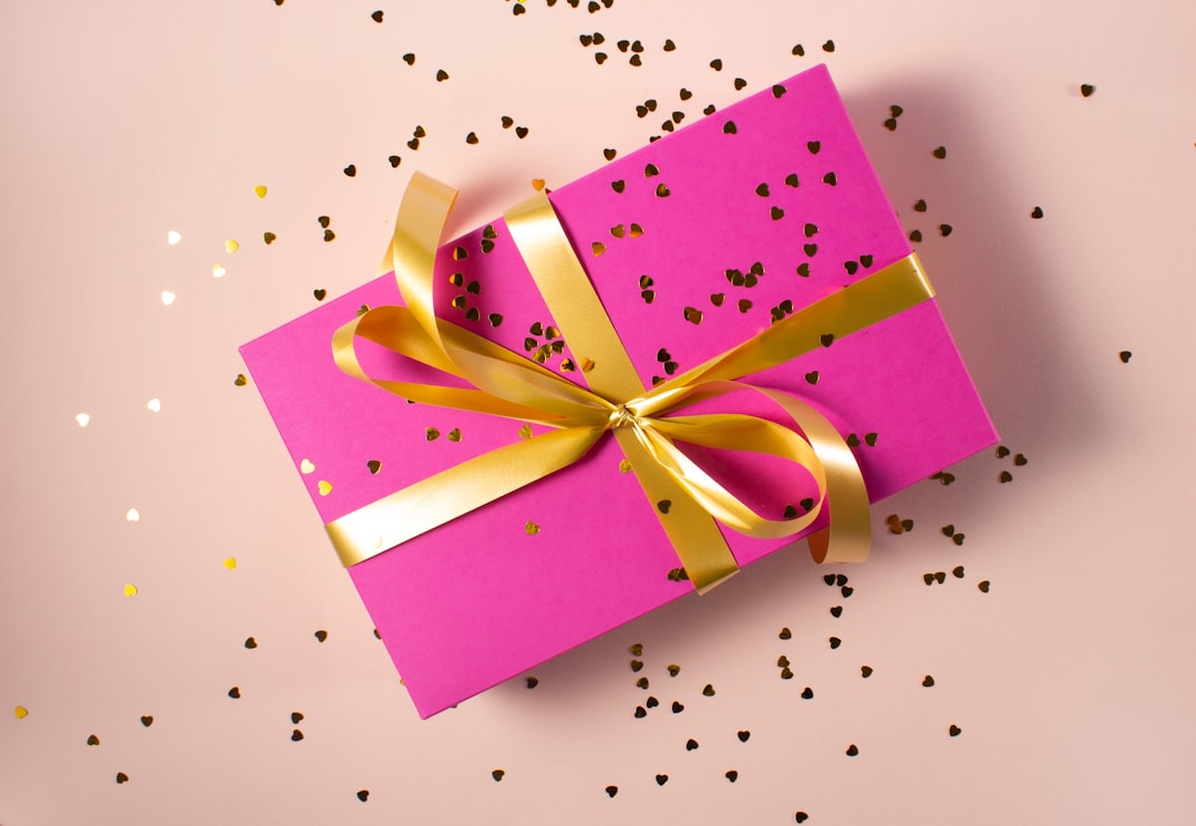 Bright pink gift box wrapped with a gold ribbon and scattered heart-shaped confetti. Bath Digital Marketing Agency