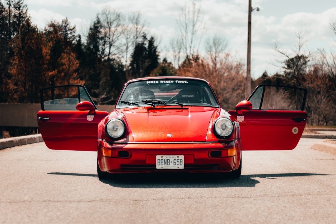 A red Porsche with open doors parked on a road, showcasing its sleek design against a backdrop of trees and a clear sky. Bath Digital Marketing Agency