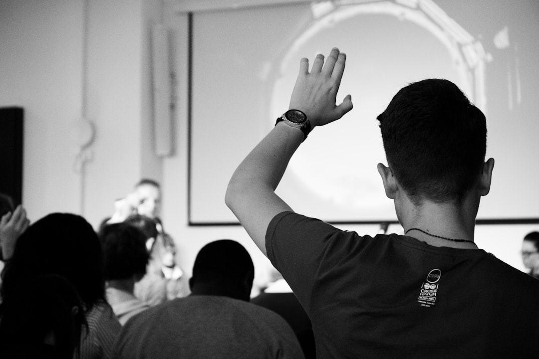 Black and white image of a person in a crowd, actively participating in a discussion or Q&A session. Bath Digital Marketing Agency