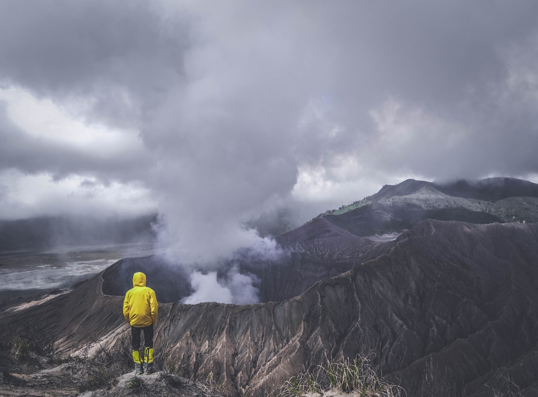 A person in a yellow raincoat standing on the edge of a volcanic crater, facing a plume of smoke rising from the volcano. Bath Digital Marketing Agency