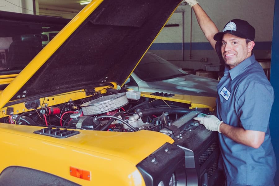 A mechanic smiling while standing next to an open yellow vehicle hood in a workshop. Bath Digital Marketing Agency