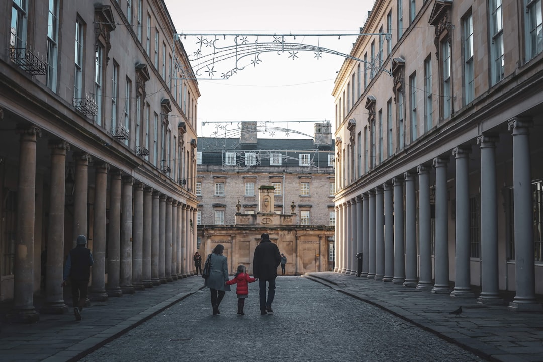 A family walking hand in hand down a cobblestone street lined with historic buildings and columns, with festive lights overhead, in the city of Bath Bath Digital Marketing Agency