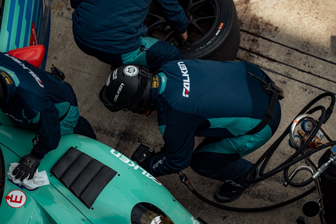 A top-down view of a racing pit crew changing a tire on a turquoise race car, with team members focused on their tasks during a pit stop. Bath Digital Marketing Agency