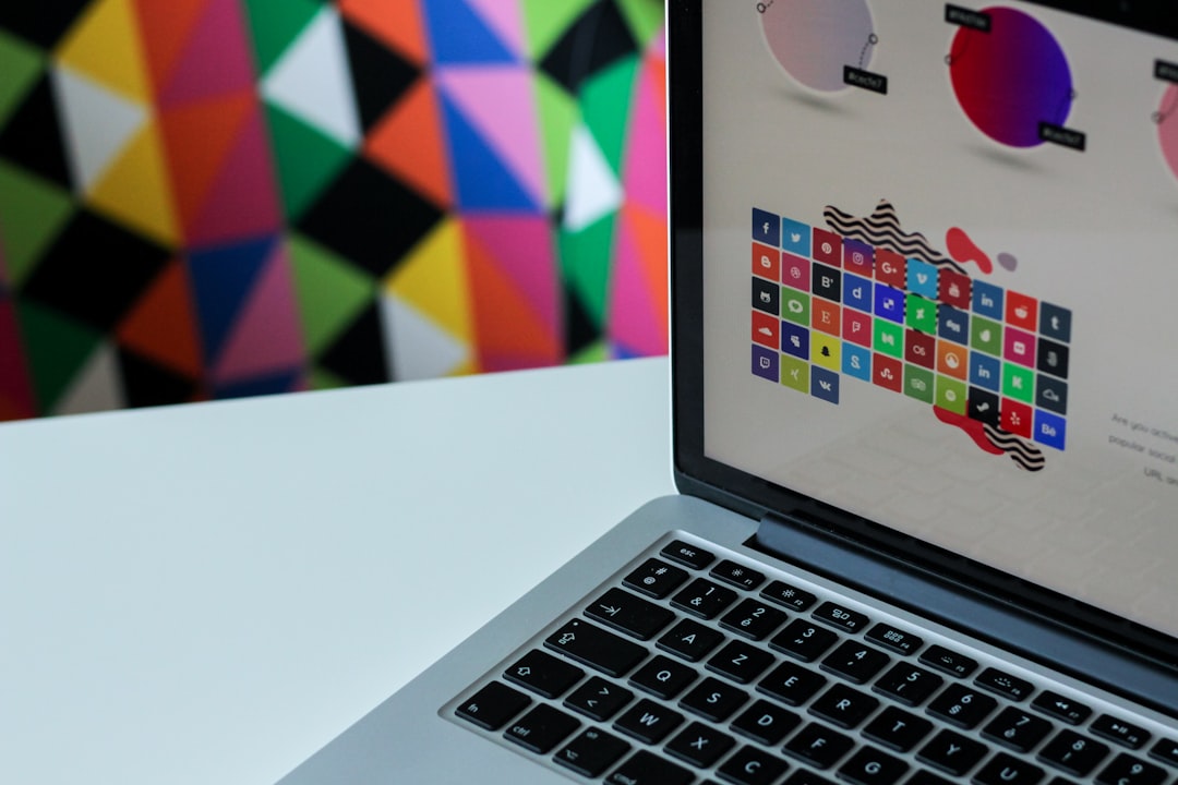 A close-up of a laptop keyboard and screen displaying a colourful design interface, with a vibrant geometric pattern in the background. Bath Digital Marketing Agency