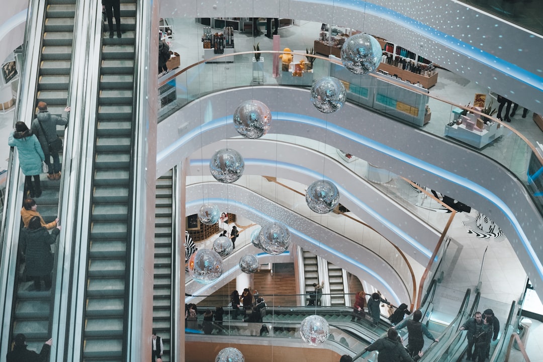 An aerial view of a modern shopping mall, showcasing escalators and shoppers. Decorative mirrored spheres hang from the ceiling, adding a festive touch to the sleek, contemporary design.  Bath Digital Marketing Agency