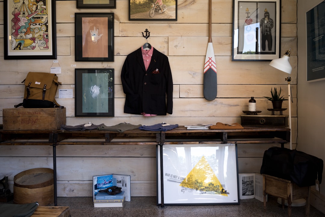 A stylish retail display featuring clothing and accessories on a wooden table. The wall behind showcases framed artwork and a paddle, while various items are neatly arranged, creating a curated and inviting atmosphere. Bath Digital Marketing Agency
