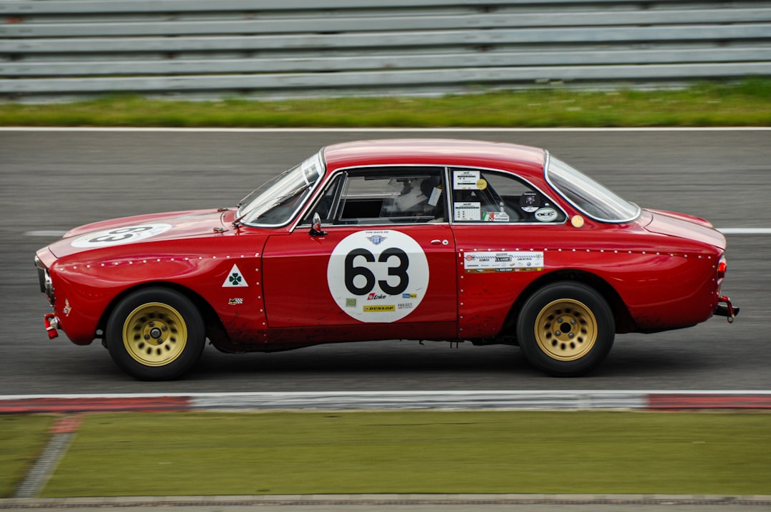 A classic red racing car with the number 63, captured in motion on a racetrack, showcasing its vintage design and sponsor logos. Bath Digital Marketing Agency