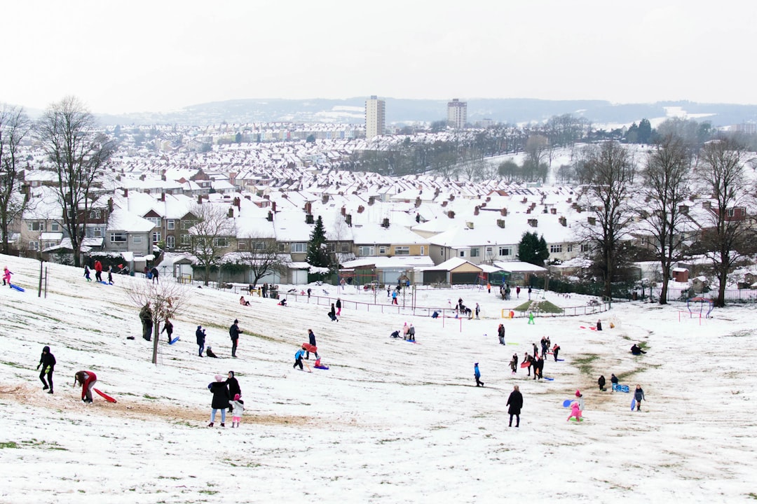 Winter scene of children and families playing in the snow on a hillside, with houses covered in snow in the background. Bath Digital Marketing Agency