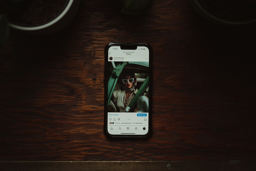 A smartphone displaying an Instagram post featuring a stylish person wearing oversized sunglasses. The phone is placed on a wooden surface, with soft lighting and plants in the background, creating a warm atmosphere. Bath Digital Marketing Agency