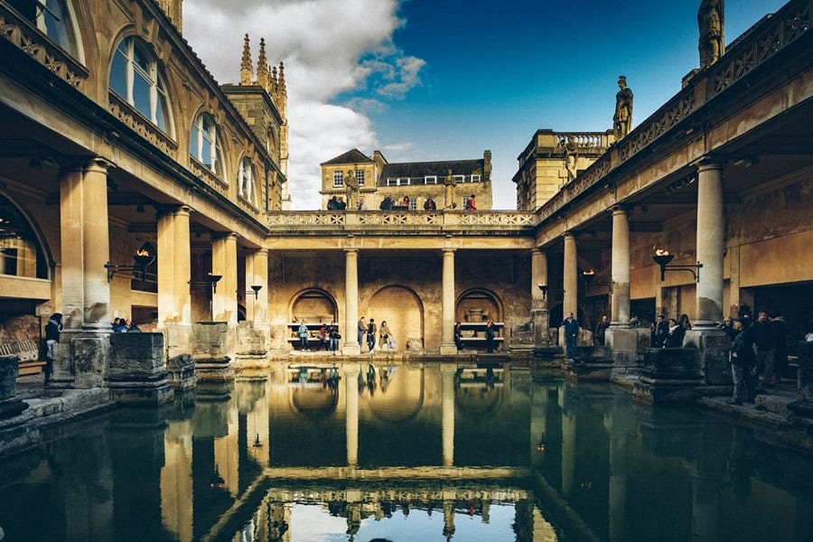 A view of the Roman Baths in Bath, England, featuring ancient columns and a reflective pool of water, with visitors exploring the historic site. Bath Digital Marketing Agency
