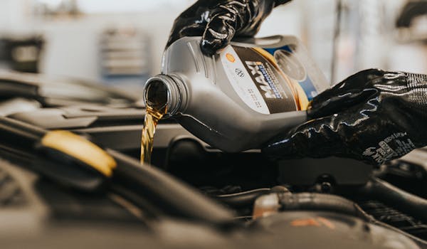 A person wearing black gloves pours engine oil into a car engine.