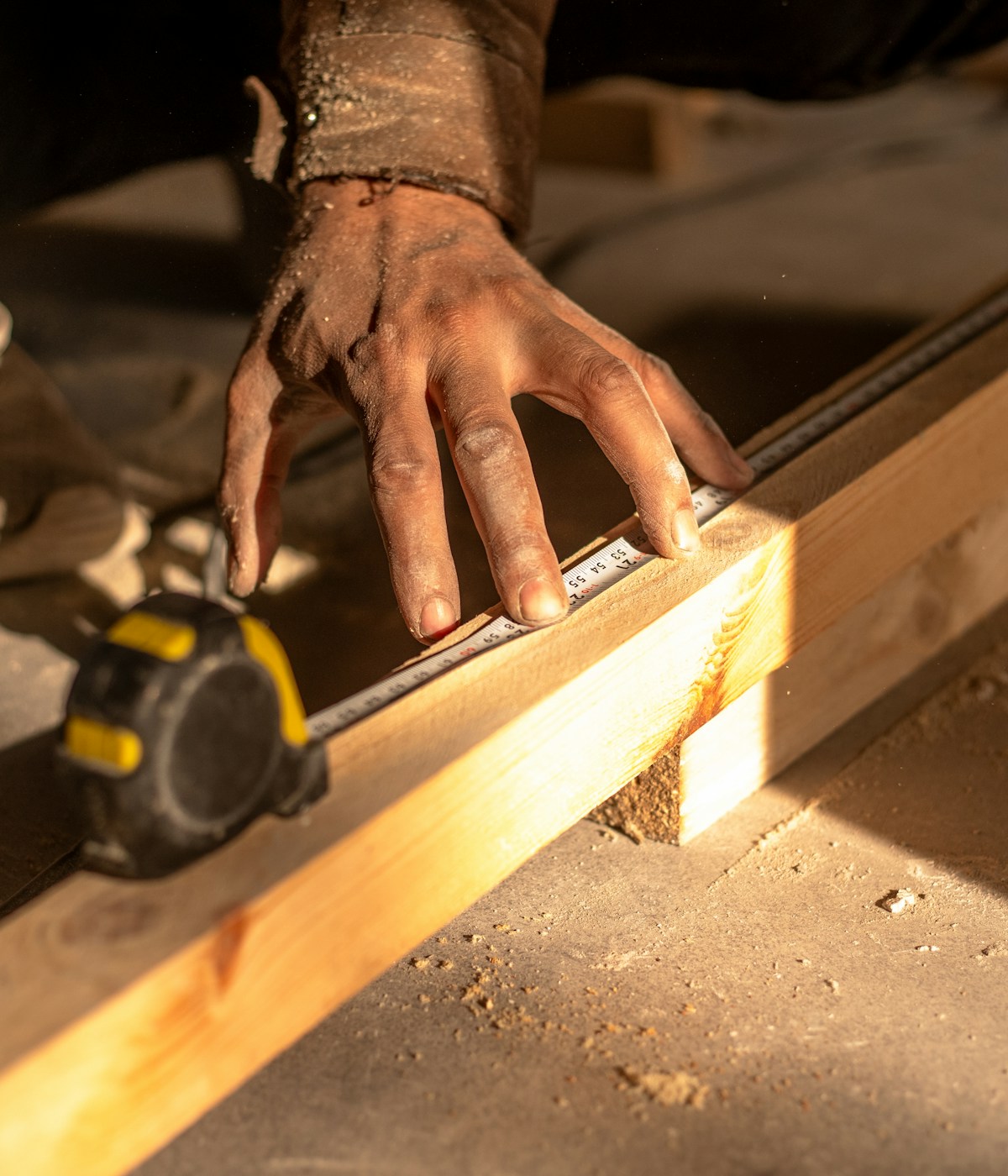 A person measuring a piece of wood with a measuring tape, focusing on accuracy and precision in their task.