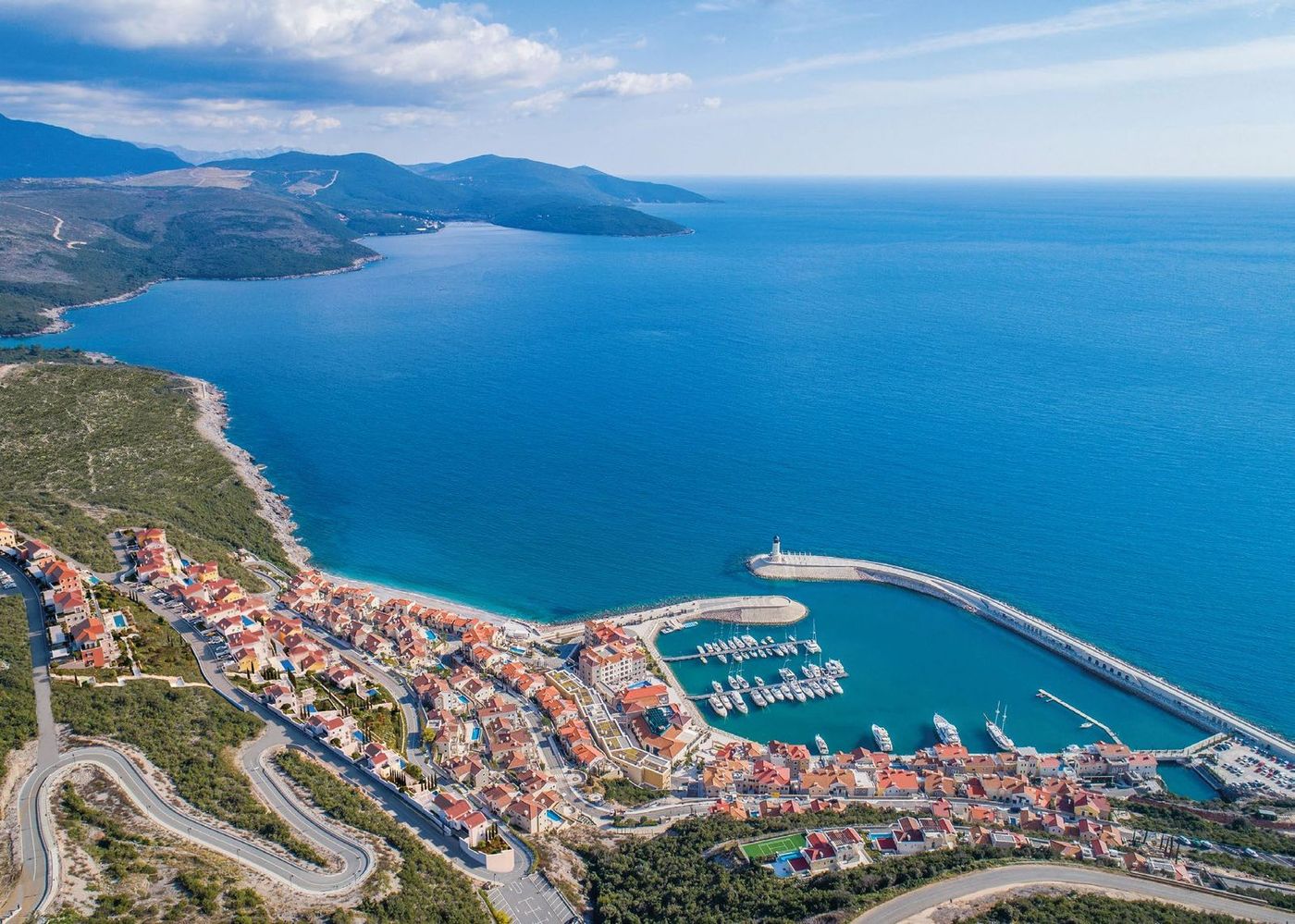 Aerial view of a marina village and green hillside on the Luštica peninsula with the open Adriatic beyond