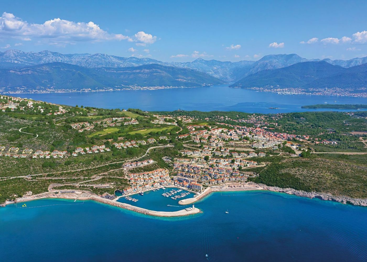 Aerial view of a coastal marina town with terracotta roofs and moored yachts on the Luštica peninsula