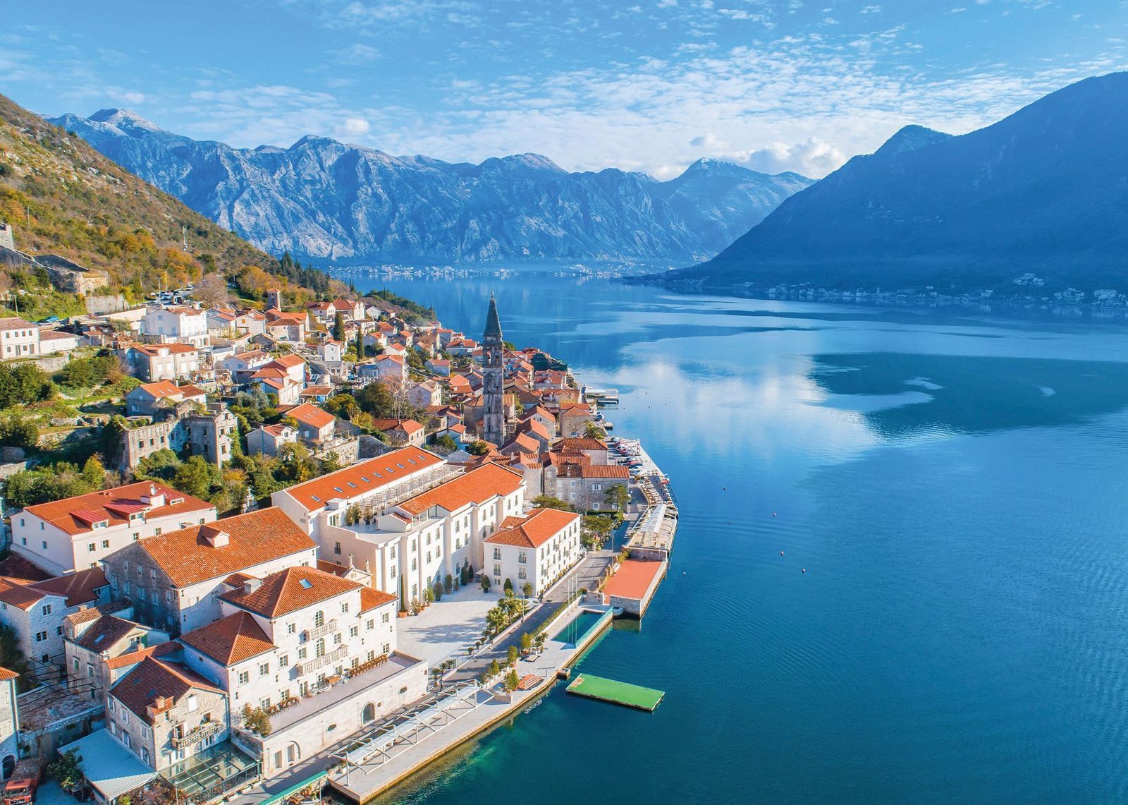 Stone town with red-tiled roofs on the shore of the Bay of Kotor, with mountains rising behind the calm water