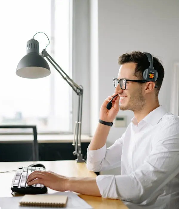 Assistant virtuel souriant utilisant un casque et un ordinateur pour fournir un support client à distance, représentant la réactivité et l'efficacité des services d'assistanat virtuel.