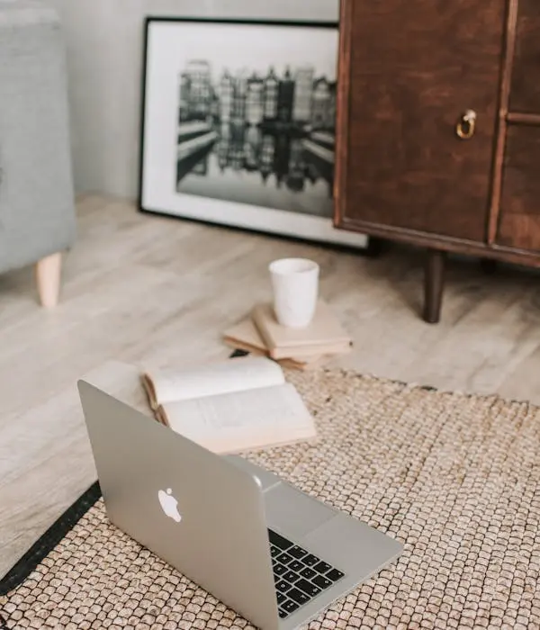 Espace de travail à domicile avec un ordinateur portable, une tasse de café et un livre ouvert, illustrant le confort et la flexibilité des services d'assistanat virtuel à distance.