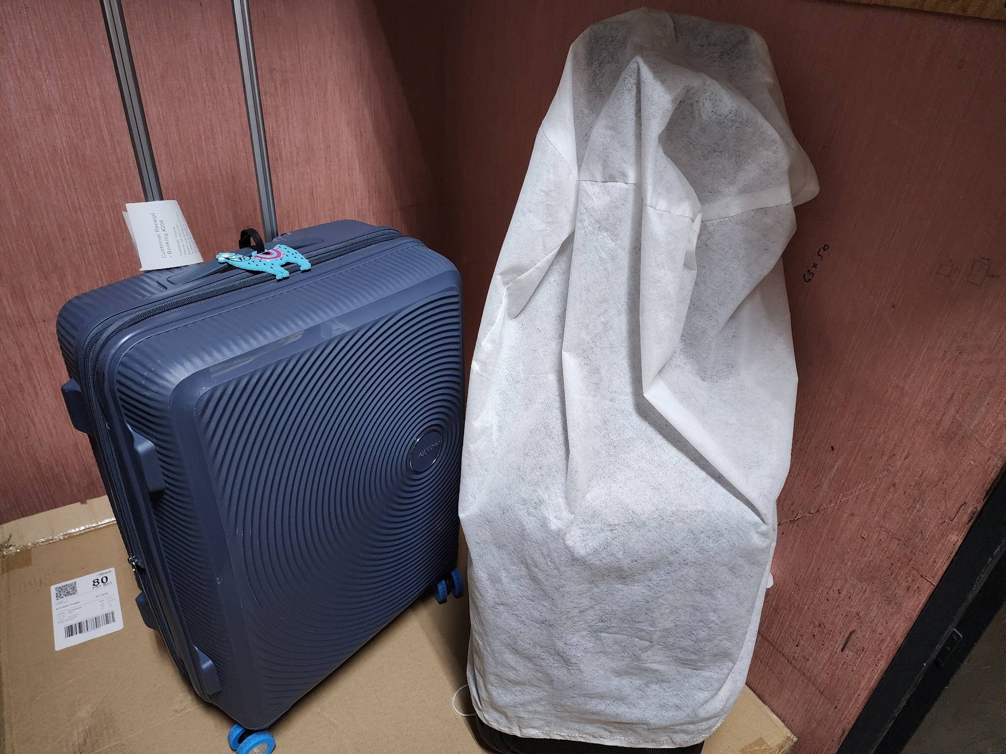 Two stored items in a luggage locker, including a blue suitcase and a covered bag, inside Luggage Locker Darwin.
