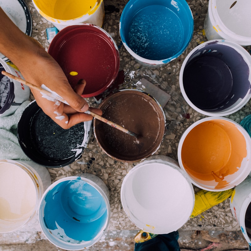 A person holds a paintbrush, applying paint to a bucket in a creative workspace.