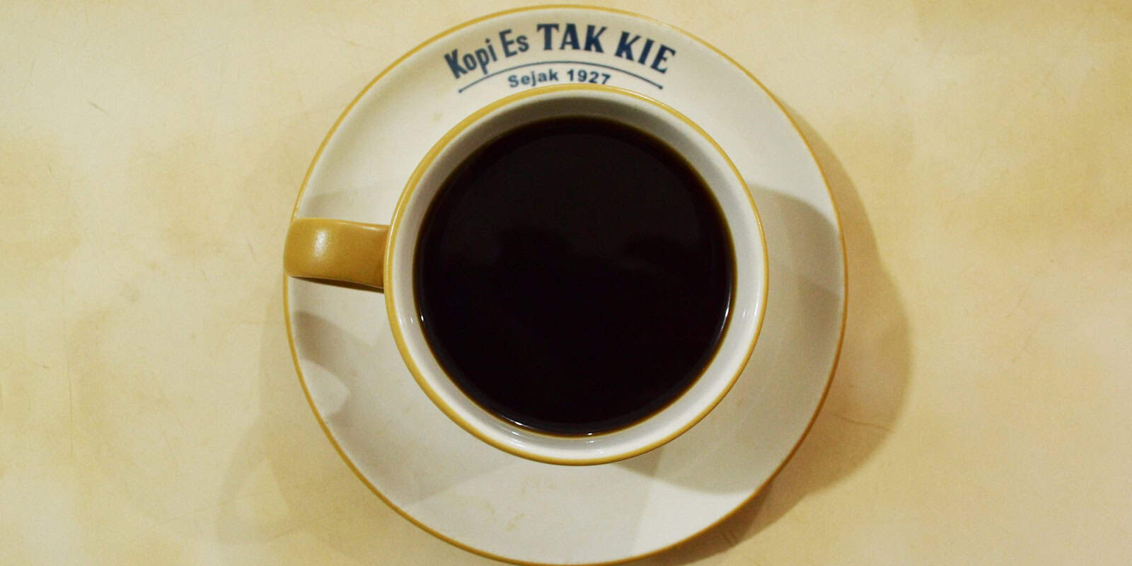 Beann Artisan Coffee" cannot be provided as the image displays a cup of black coffee from "Kopi Es Tak Kie" - beann speciality coffee