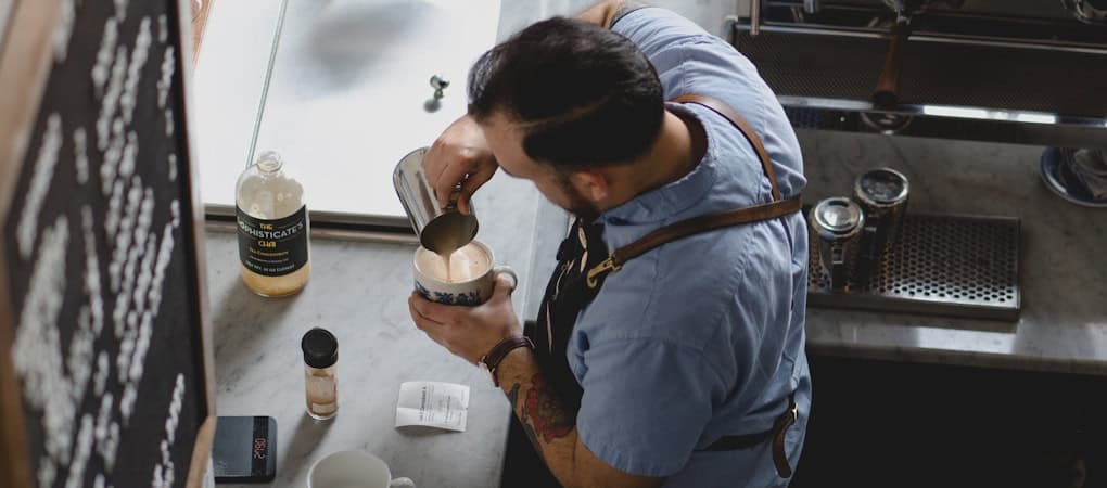 A barista pouring steamed milk into a coffee cup to create latte art - beann artisan coffee