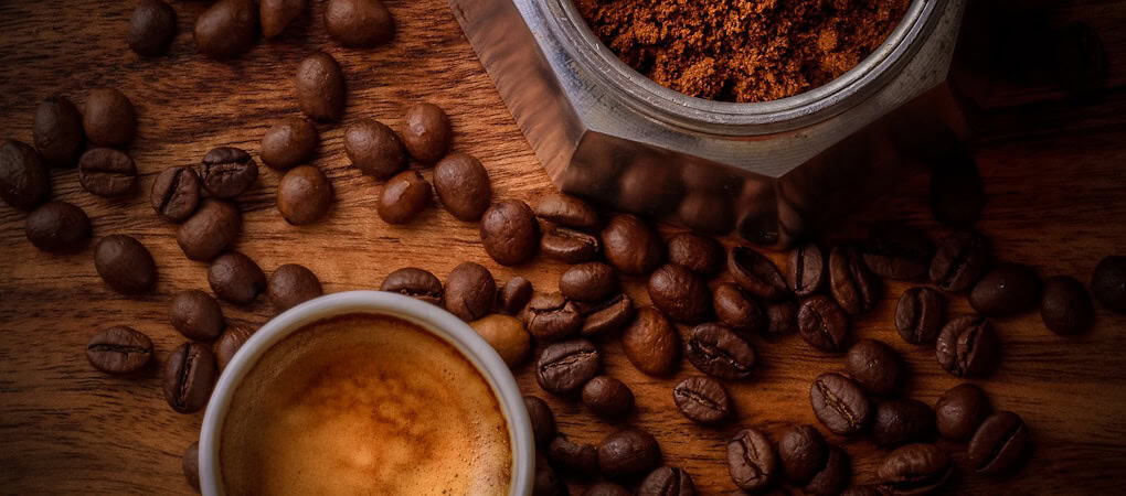 Roasted coffee beans, a small cup of espresso, and ground coffee in a moka pot on a wooden table - beann artisan coffee