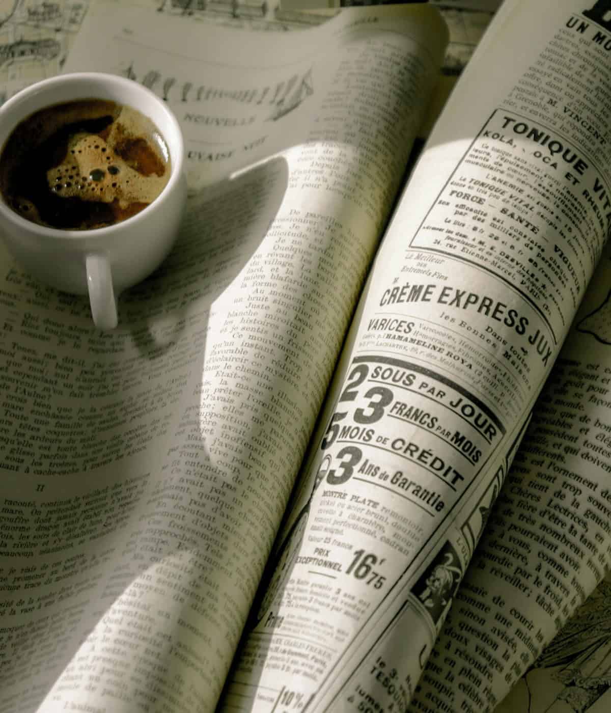 A white ceramic cup filled with dark, freshly brewed Beann artisan coffee, sitting on a newspaper on a table - beann speciality coffee