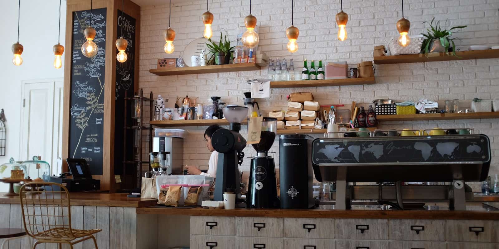 Interior of a cozy, modern artisan coffee shop with an espresso machine, wooden shelves, and a barista behind the counter - beann speciality coffee
