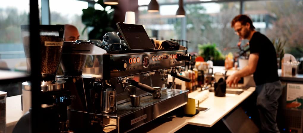 A barista preparing coffee behind a counter with a La Marzocco espresso machine and coffee grinders - beann artisan coffee