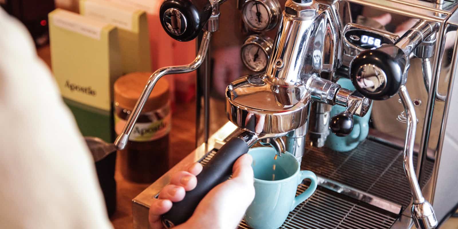 Close-up of a person pulling an espresso shot into a light blue mug using a chrome espresso machine - beann artisan coffee